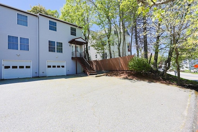 rear view of house featuring an attached garage, fence, and aphalt driveway
