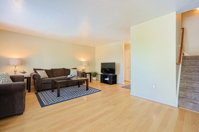 living room featuring baseboards, light wood finished floors, and stairs