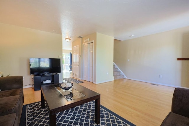 living area with stairs, baseboards, visible vents, and wood finished floors
