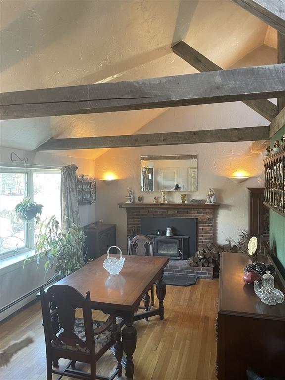 dining space featuring hardwood / wood-style flooring, lofted ceiling with beams, and a brick fireplace