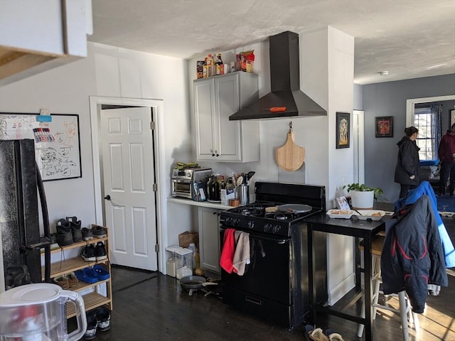 kitchen featuring gas stove, light countertops, wall chimney range hood, and wood finished floors