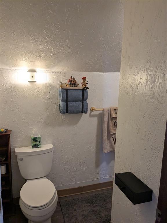 half bathroom with toilet, baseboards, and a textured wall