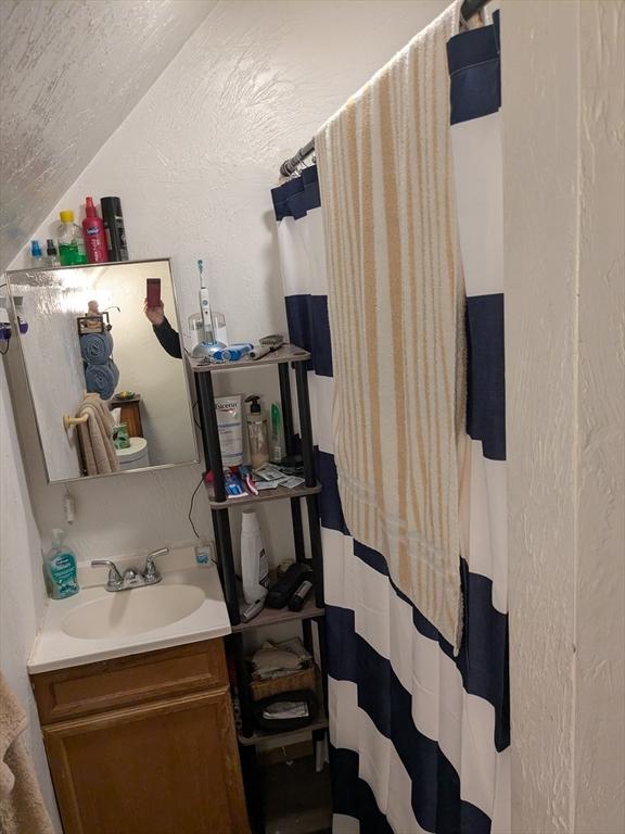 bathroom featuring lofted ceiling, a textured wall, a shower with shower curtain, and vanity