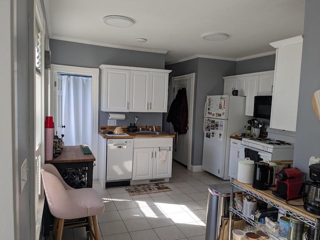 kitchen with white appliances, light tile patterned floors, ornamental molding, white cabinetry, and a sink