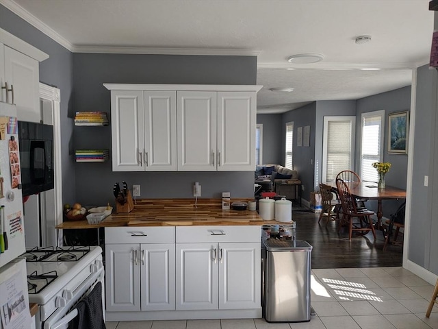 kitchen featuring black microwave, butcher block counters, crown molding, white cabinetry, and gas range gas stove