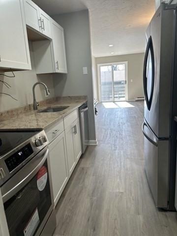 kitchen with light wood finished floors, light stone counters, appliances with stainless steel finishes, white cabinetry, and a sink