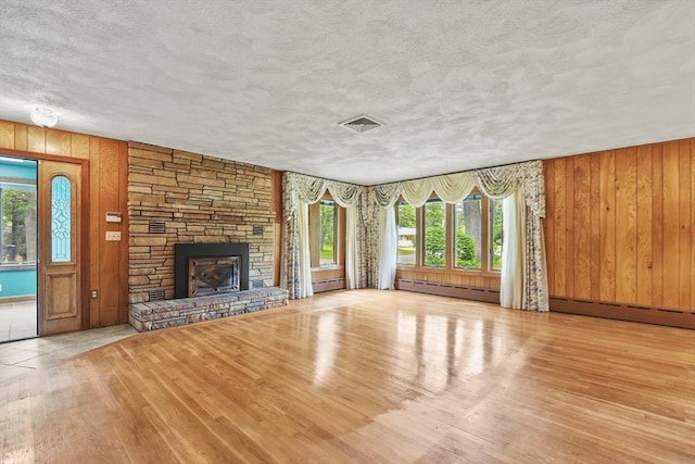 210 Plain Dr, Stoughton, MA 02072 - unfurnished living room with baseboard heating, hardwood / wood-style flooring, a textured ceiling, wooden walls, and a stone fireplace