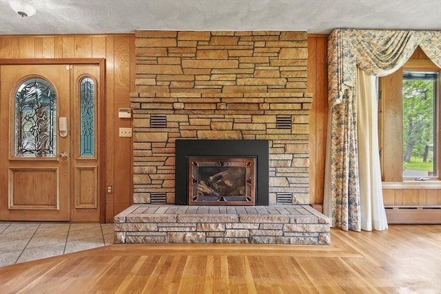 210 Plain Dr, Stoughton, MA 02072 - unfurnished living room featuring a fireplace, a baseboard heating unit, wood finished floors, wood walls, and a textured ceiling