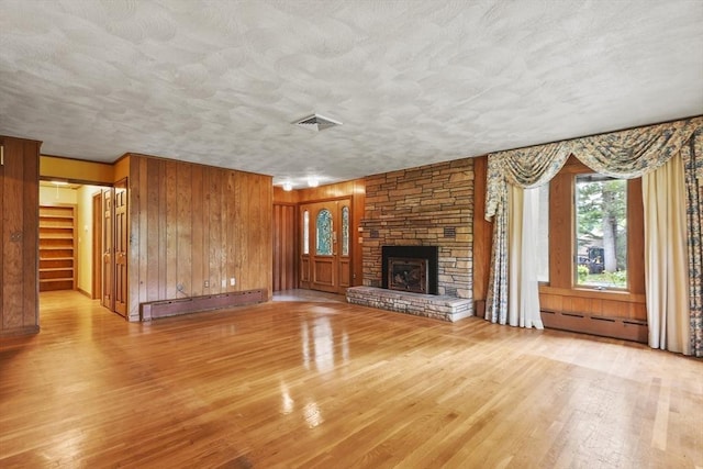 210 Plain Dr, Stoughton, MA 02072 - unfurnished living room featuring a baseboard heating unit, wood finished floors, a fireplace, wood walls, and a textured ceiling