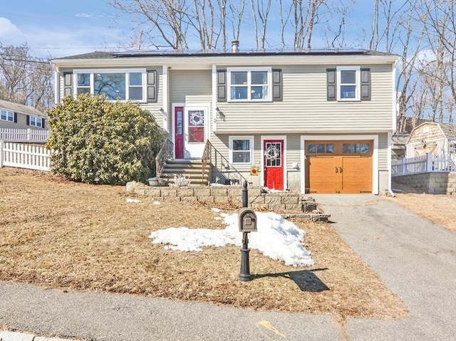 split foyer home featuring fence, aphalt driveway, entry steps, roof mounted solar panels, and an attached garage