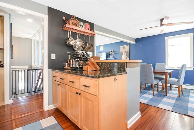 kitchen featuring light brown cabinetry, dark stone countertops, dark wood-type flooring, and a ceiling fan