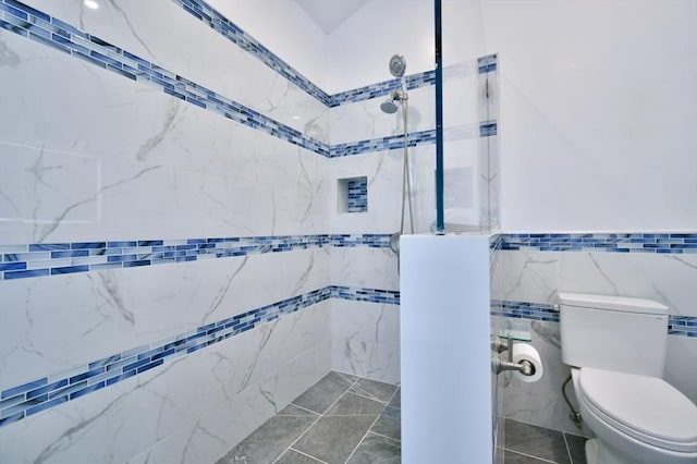 full bathroom with a tile shower, toilet, and tile walls