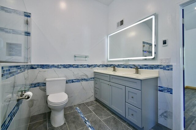 bathroom with tile walls, toilet, double vanity, and wainscoting