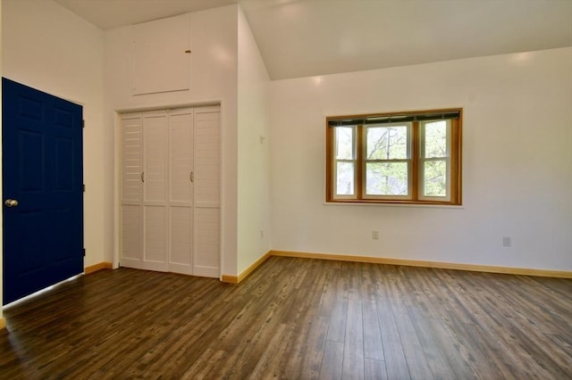 unfurnished bedroom with dark wood finished floors, a closet, baseboards, and vaulted ceiling