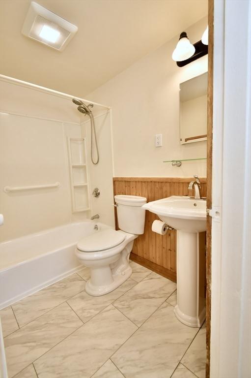 bathroom with toilet, wainscoting, wood walls, shower / tub combination, and a sink
