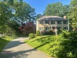 colonial house with aphalt driveway, a chimney, and a front lawn