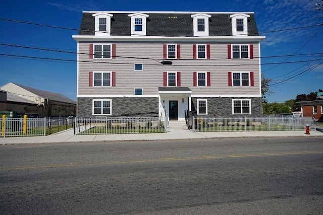 victorian home with a fenced front yard, stone siding, roof with shingles, and mansard roof