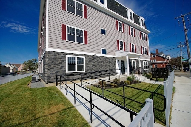 view of front of property featuring stone siding, central AC, a front yard, and fence