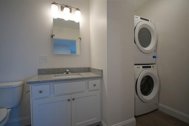 washroom with dark wood-style floors, a sink, stacked washing maching and dryer, laundry area, and baseboards