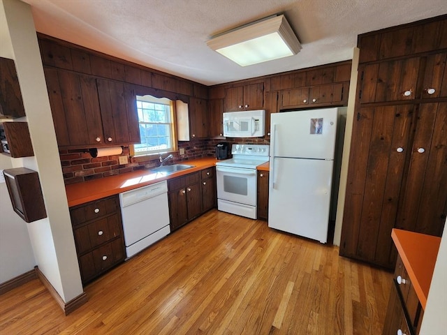 kitchen with dark brown cabinets, light hardwood / wood-style floors, white appliances, and sink