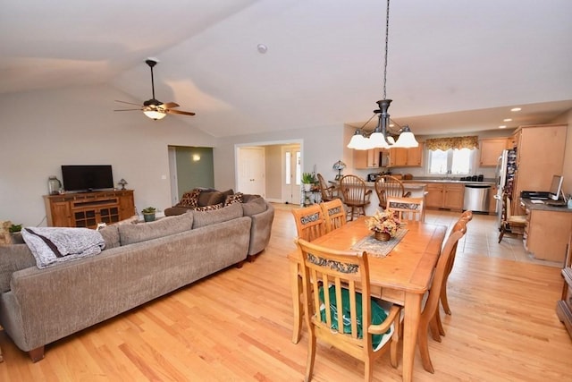 dining space featuring ceiling fan with notable chandelier, vaulted ceiling, and light hardwood / wood-style floors