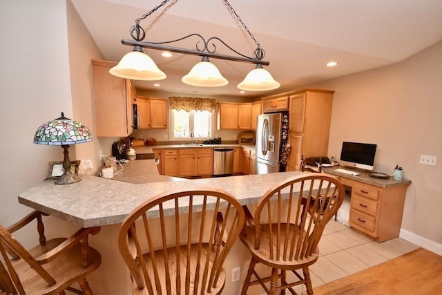 kitchen with stainless steel appliances, kitchen peninsula, a kitchen bar, light brown cabinetry, and light tile patterned flooring