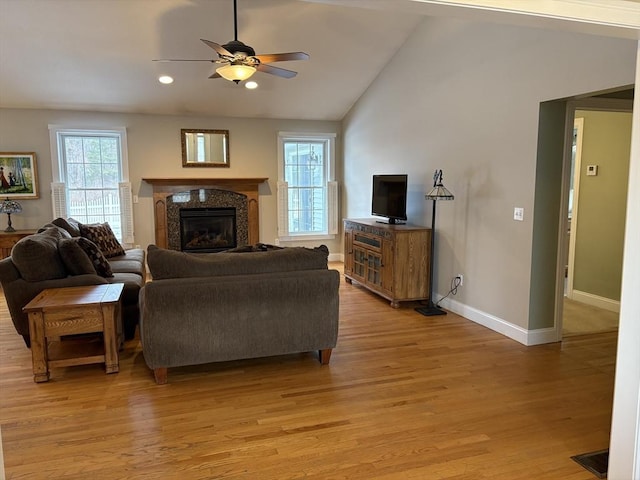 living room with a high end fireplace, ceiling fan, vaulted ceiling, and light hardwood / wood-style flooring