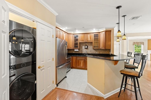 190 Chickering Rd Unit 201D, North Andover, MA 01845 - kitchen featuring appliances with stainless steel finishes, stacked washer / drying machine, brown cabinetry, ornamental molding, and a breakfast bar