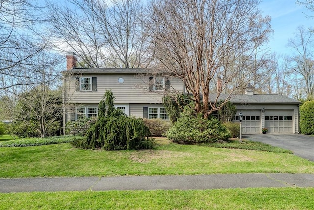 view of front of property featuring a chimney, an attached garage, a front lawn, and aphalt driveway