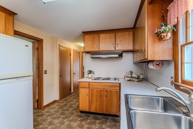 kitchen with white appliances, light countertops, under cabinet range hood, dark floors, and a sink