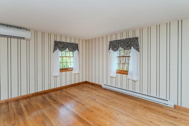 empty room with wood finished floors, a wall unit AC, and baseboard heating
