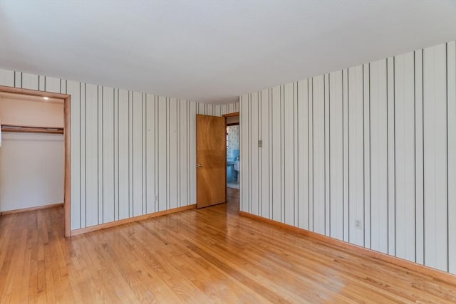 unfurnished bedroom with a closet, wood finished floors, baseboards, a walk in closet, and wallpapered walls