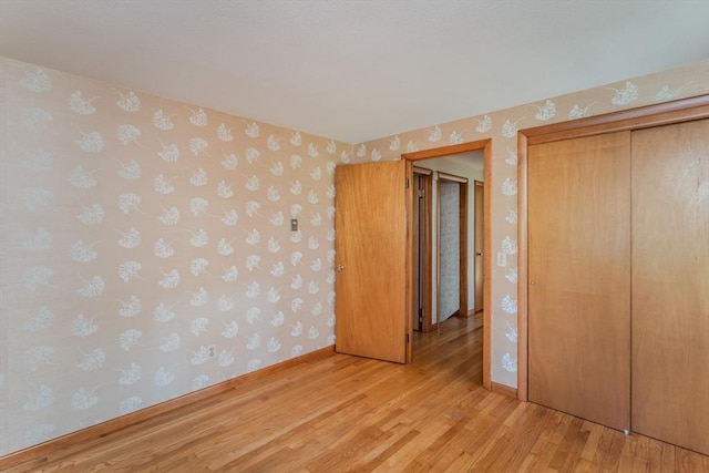unfurnished bedroom with baseboards, wallpapered walls, light wood-style flooring, and a closet