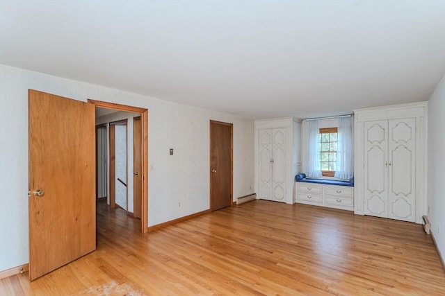 unfurnished bedroom featuring baseboards, light wood finished floors, multiple closets, and baseboard heating