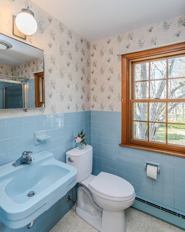 bathroom featuring a stall shower, a sink, a baseboard radiator, toilet, and wallpapered walls