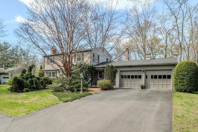 traditional-style home with an attached garage, aphalt driveway, a front yard, and a chimney