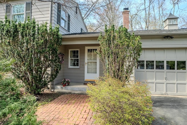 view of exterior entry with an attached garage, aphalt driveway, and a chimney