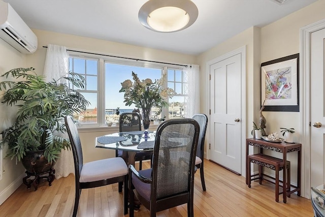 dining space featuring light wood-style floors, baseboards, and a wall mounted air conditioner