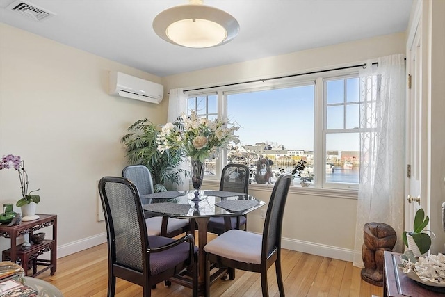 dining room with light wood-type flooring, an AC wall unit, visible vents, and baseboards