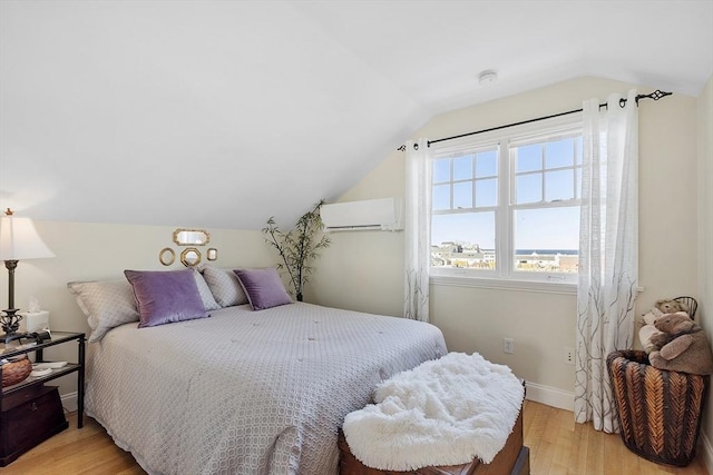 bedroom with vaulted ceiling, light wood finished floors, a wall mounted AC, and baseboards