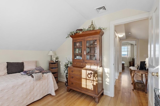 bedroom with light wood-style floors, baseboards, visible vents, and vaulted ceiling