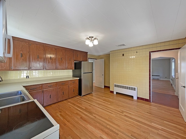 kitchen with stainless steel fridge, sink, radiator heating unit, tasteful backsplash, and light hardwood / wood-style flooring