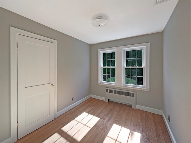 spare room featuring radiator heating unit and light hardwood / wood-style floors