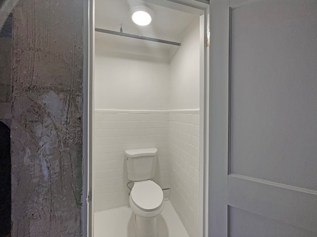 bathroom featuring tile walls, toilet, and a shower