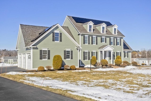 view of front facade with driveway, a shingled roof, roof mounted solar panels, and a garage