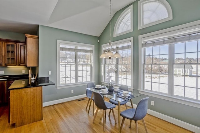 dining area with light wood finished floors, baseboards, visible vents, and vaulted ceiling