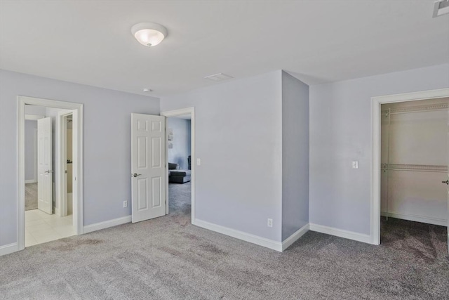 unfurnished bedroom with carpet, visible vents, baseboards, and a walk in closet