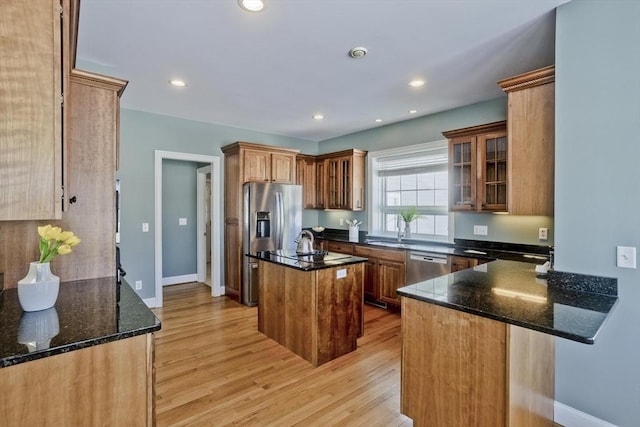 kitchen featuring light wood finished floors, dark stone counters, appliances with stainless steel finishes, a kitchen island with sink, and recessed lighting