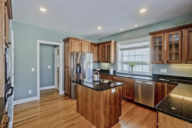 kitchen featuring dark stone counters, light wood-style flooring, appliances with stainless steel finishes, a center island, and a sink