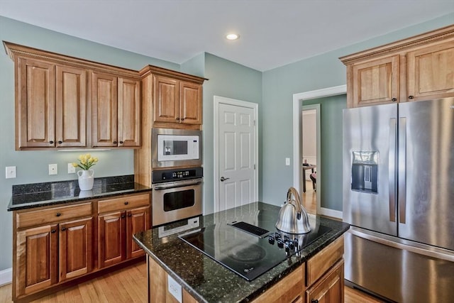 kitchen with brown cabinetry, light wood-style flooring, appliances with stainless steel finishes, dark stone countertops, and recessed lighting